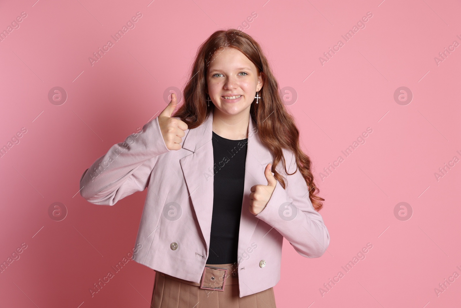 Photo of Smiling teenage girl showing thumbs up on pink background