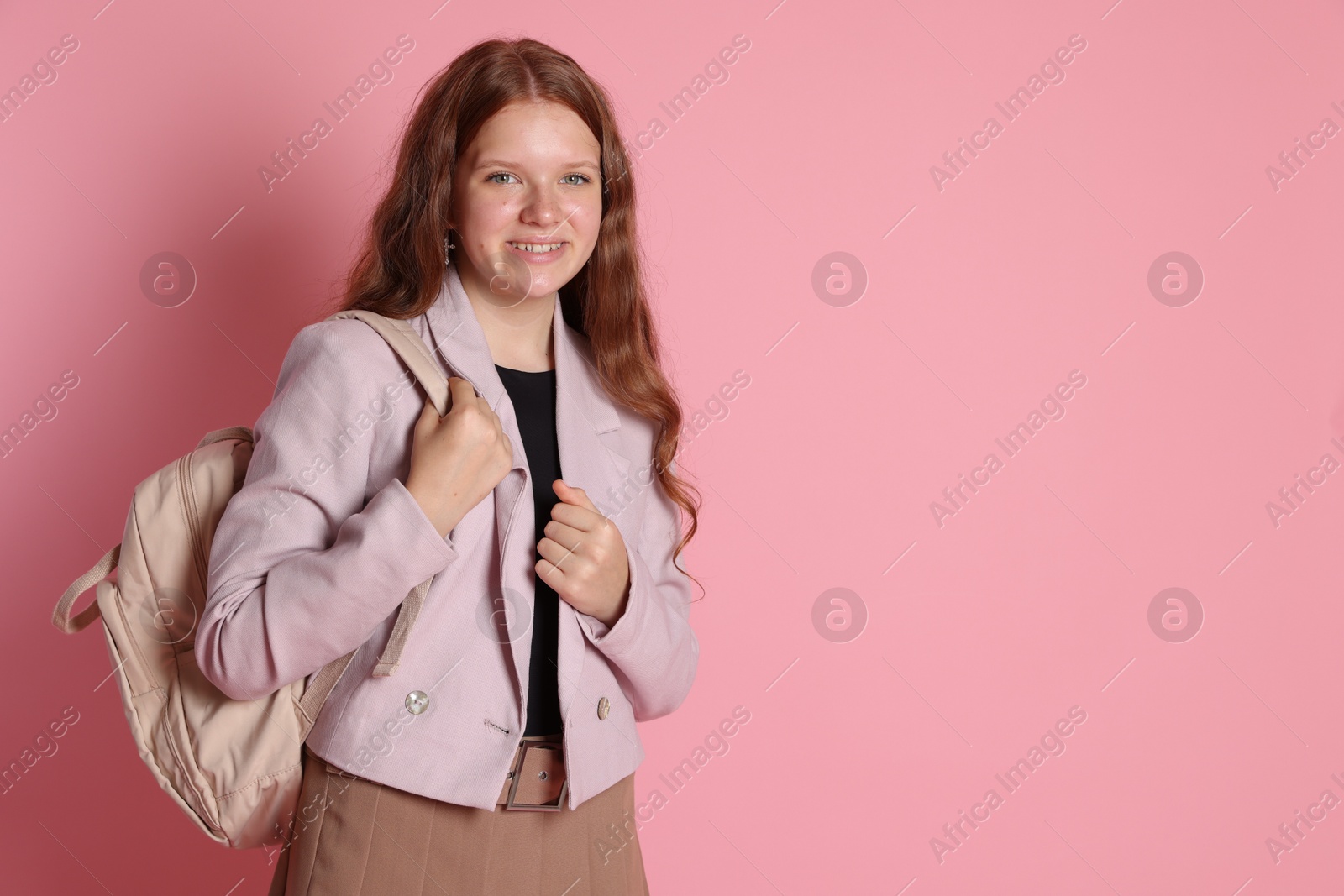 Photo of Smiling teenage girl with backpack on pink background. Space for text