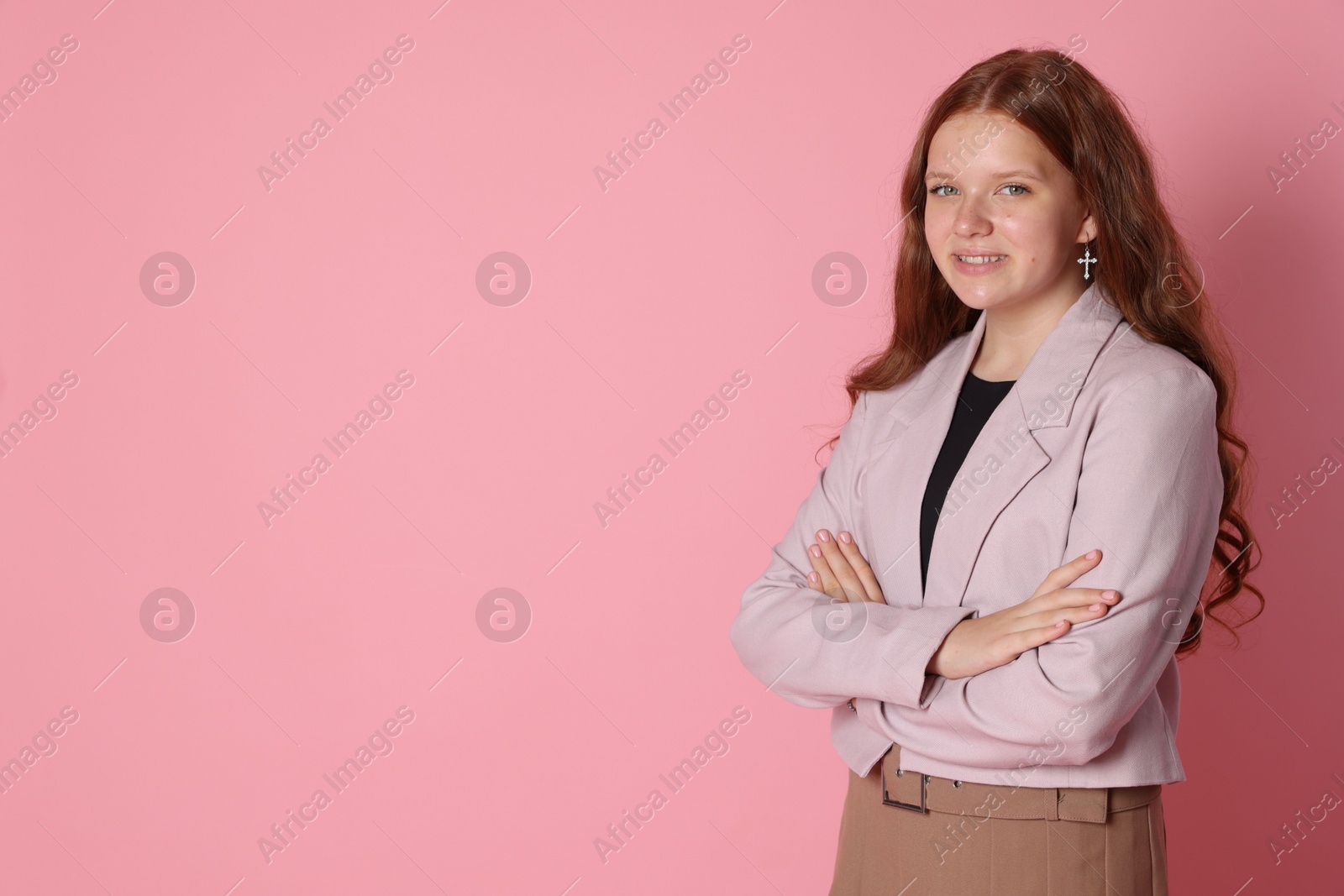 Photo of Smiling teenage girl with crossed arms on pink background. Space for text