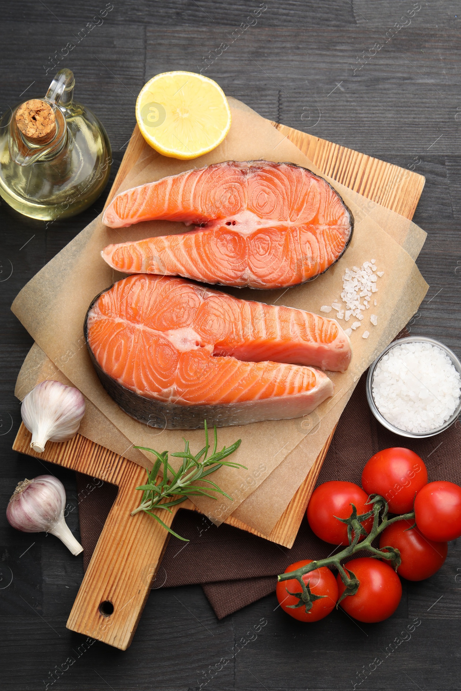 Photo of Fresh raw salmon steaks and products on black wooden table, flat lay