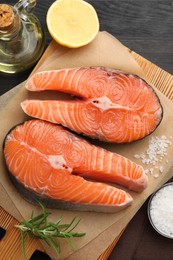 Photo of Fresh raw salmon steaks and spices on black wooden table, flat lay