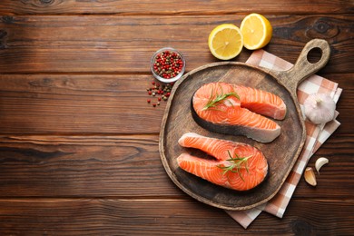 Photo of Fresh raw salmon steaks and spices on wooden table, flat lay. Space for text