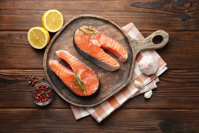 Photo of Fresh raw salmon steaks and spices on wooden table, flat lay