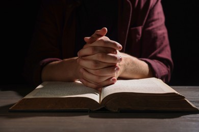 Photo of Man with Bible praying at wooden table, closeup