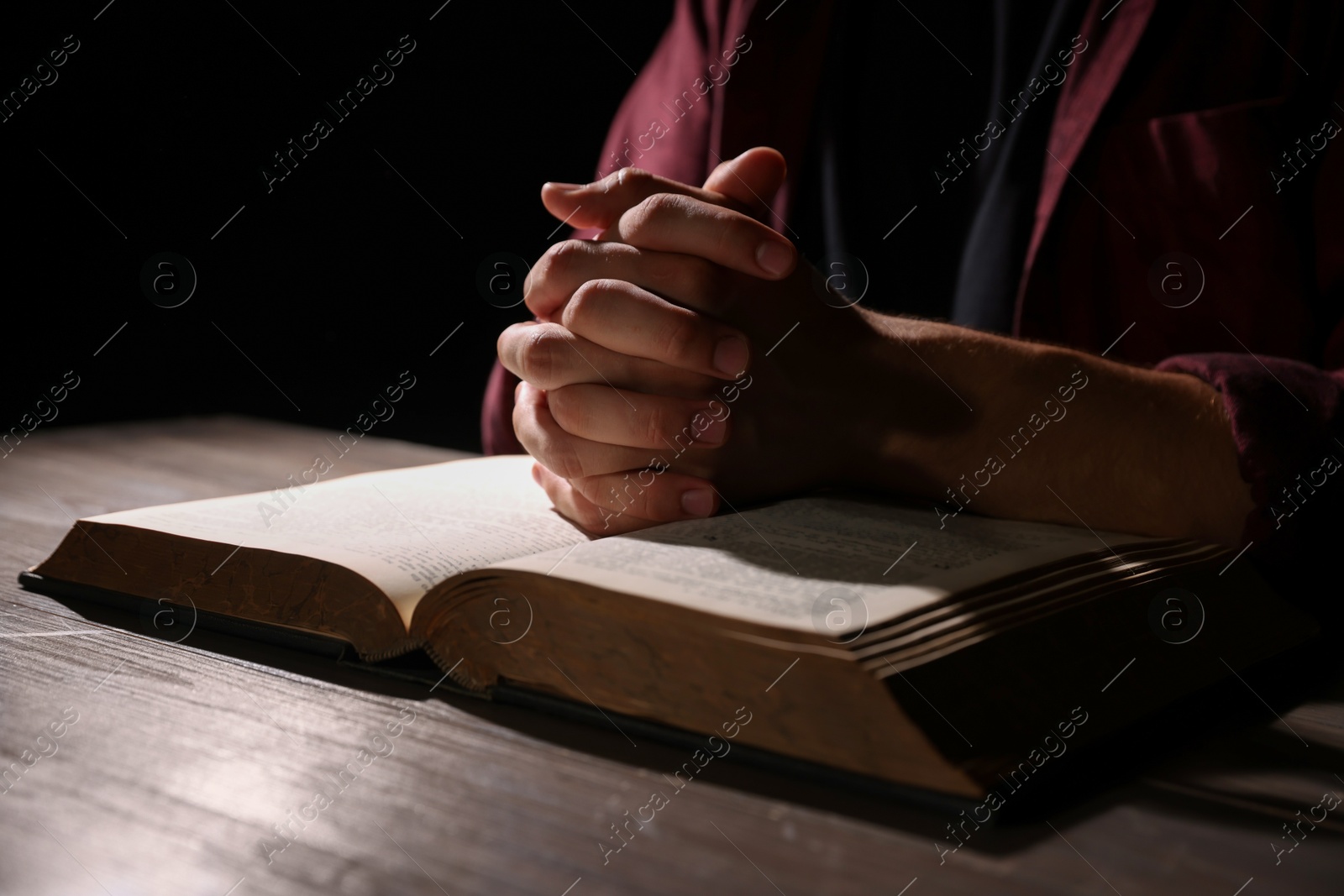 Photo of Man with Bible praying at wooden table, closeup