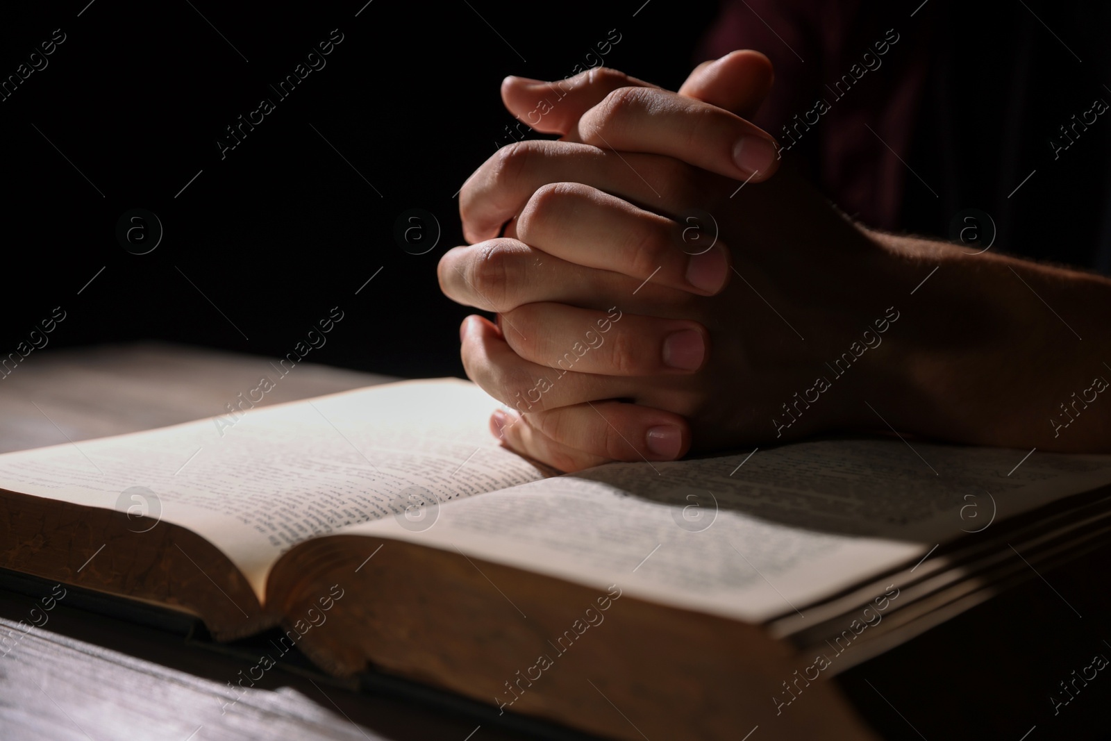 Photo of Man with Bible praying at wooden table, closeup