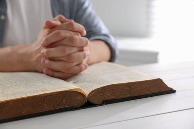 Photo of Man with Bible praying at white wooden table, closeup