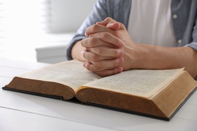 Photo of Man with Bible praying at white wooden table, closeup