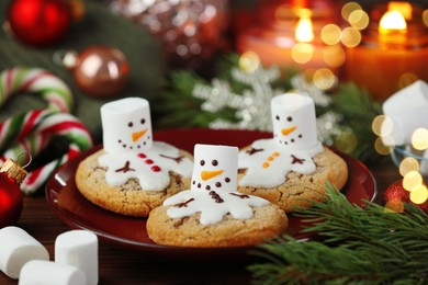 Photo of Funny marshmallow snowmen, cookies and festive decor on table, closeup