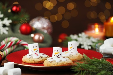 Photo of Funny marshmallow snowmen, cookies and festive decor on table, closeup