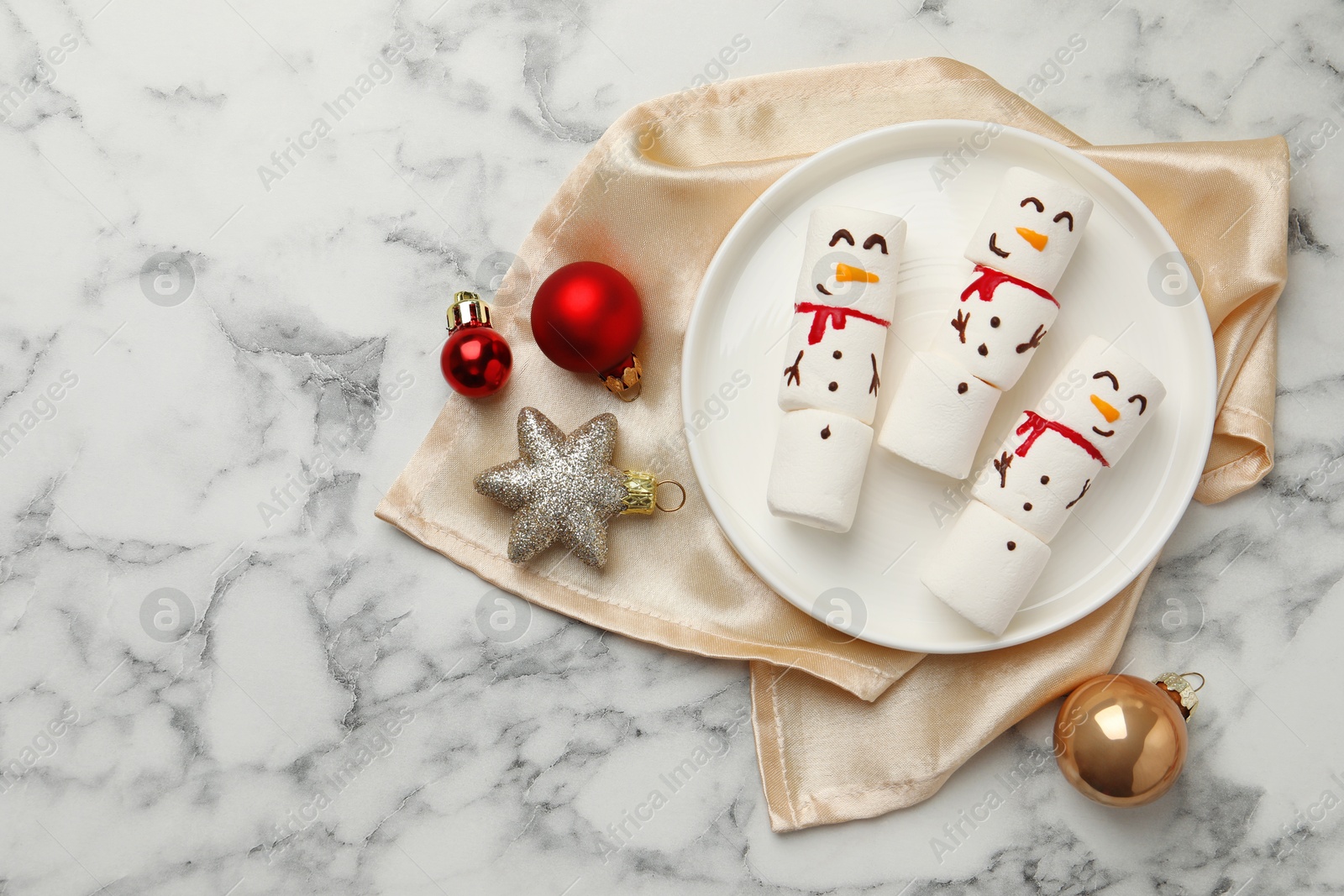 Photo of Funny marshmallow snowmen and festive decor on white marble table, top view