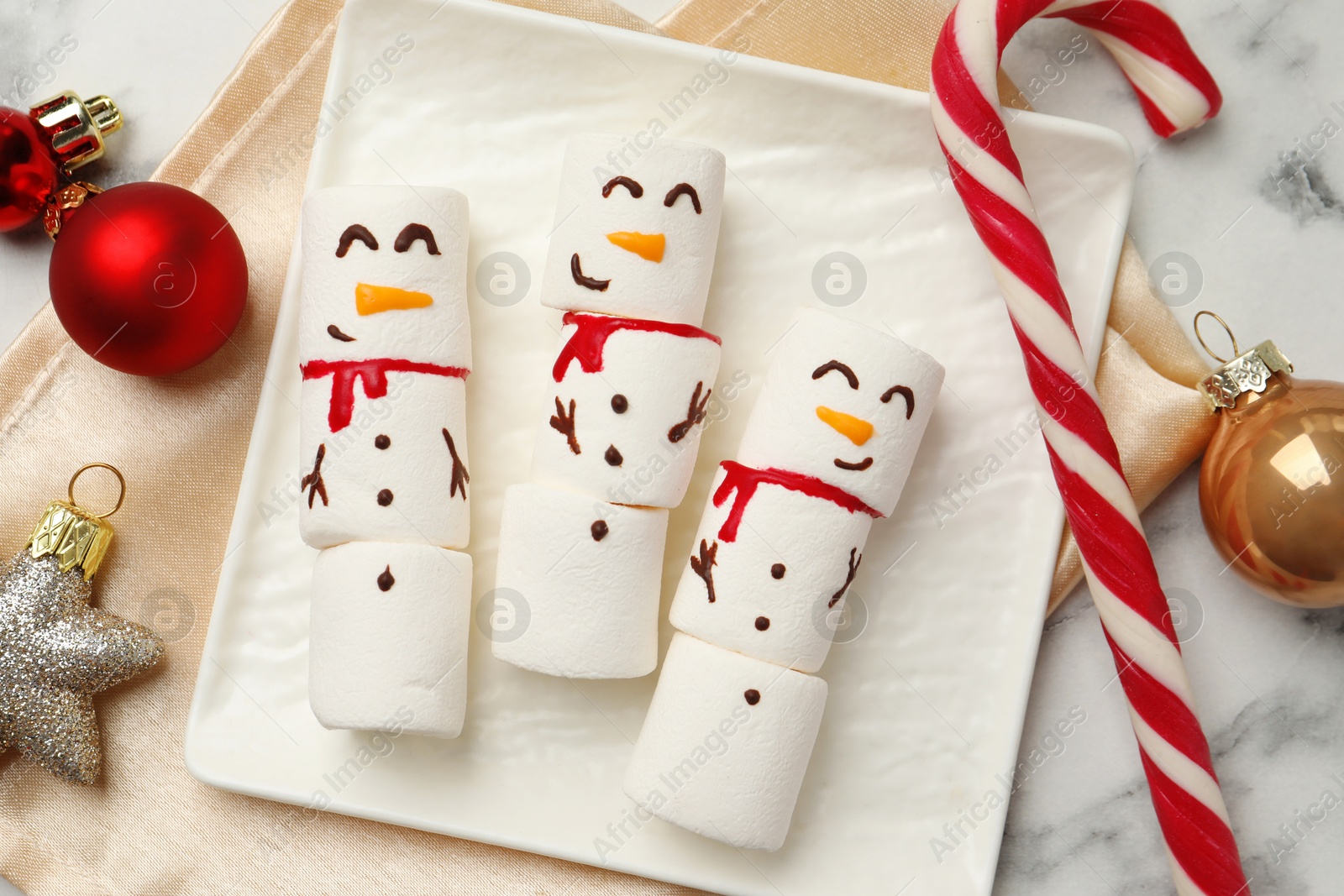 Photo of Funny marshmallow snowmen and festive decor on white marble table, top view