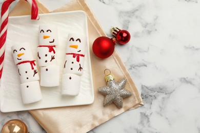 Funny marshmallow snowmen and festive decor on white marble table, top view