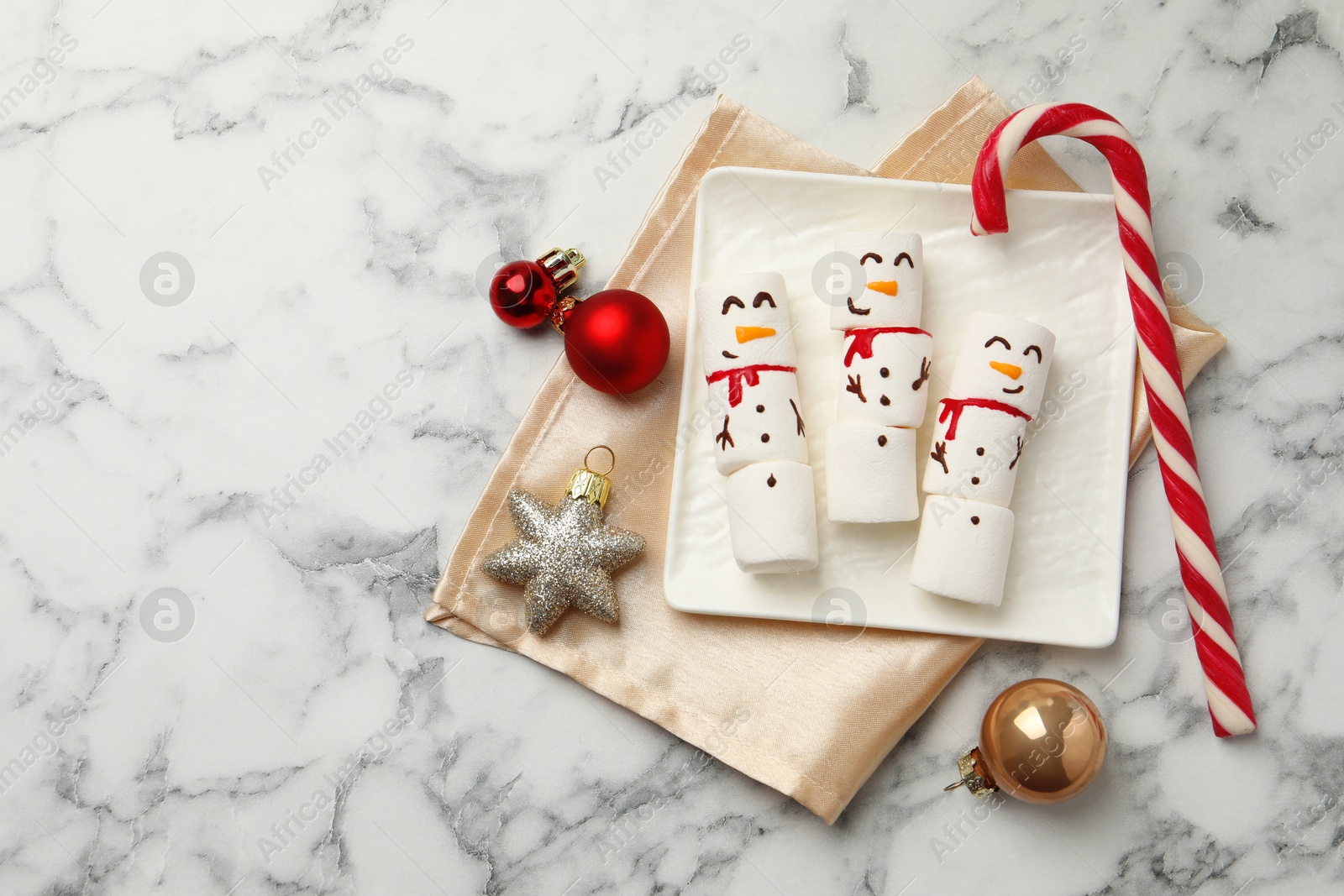 Photo of Funny marshmallow snowmen and festive decor on white marble table, top view. Space for text