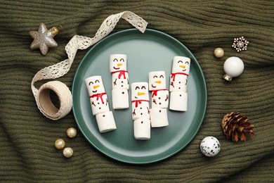 Photo of Funny marshmallow snowmen and festive decor on olive knitted fabric, top view