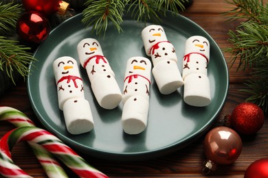 Photo of Funny marshmallow snowmen and festive decor on wooden table, closeup