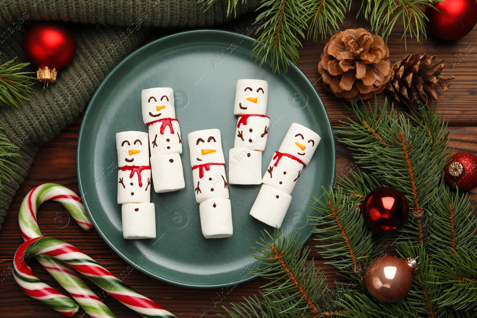 Photo of Funny marshmallow snowmen and festive decor on wooden table, flat lay