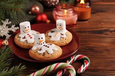 Photo of Funny marshmallow snowmen, cookies and festive decor on wooden table, closeup