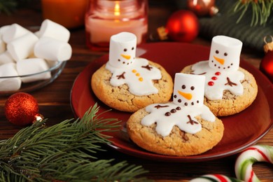 Photo of Funny marshmallow snowmen, cookies and festive decor on wooden table, closeup