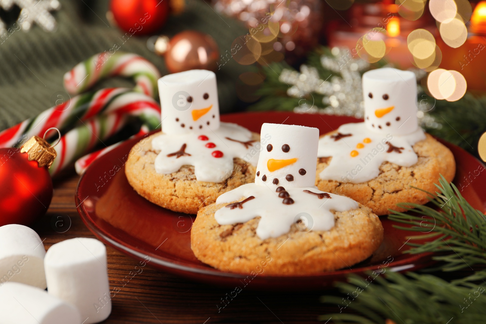 Photo of Funny marshmallow snowmen, cookies and festive decor on wooden table, closeup