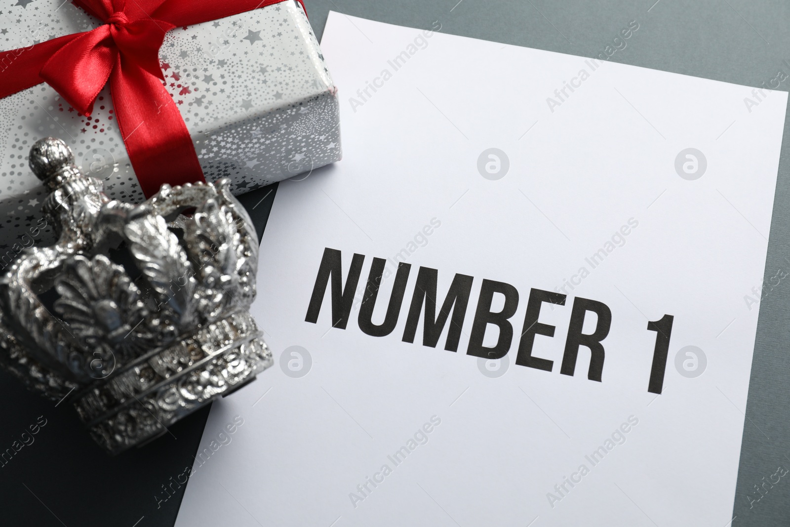 Photo of Sheet of paper with word Number 1, gift box and silver crown on grey table, above view