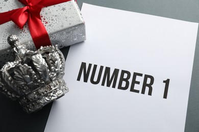 Photo of Sheet of paper with word Number 1, gift box and silver crown on grey table, above view