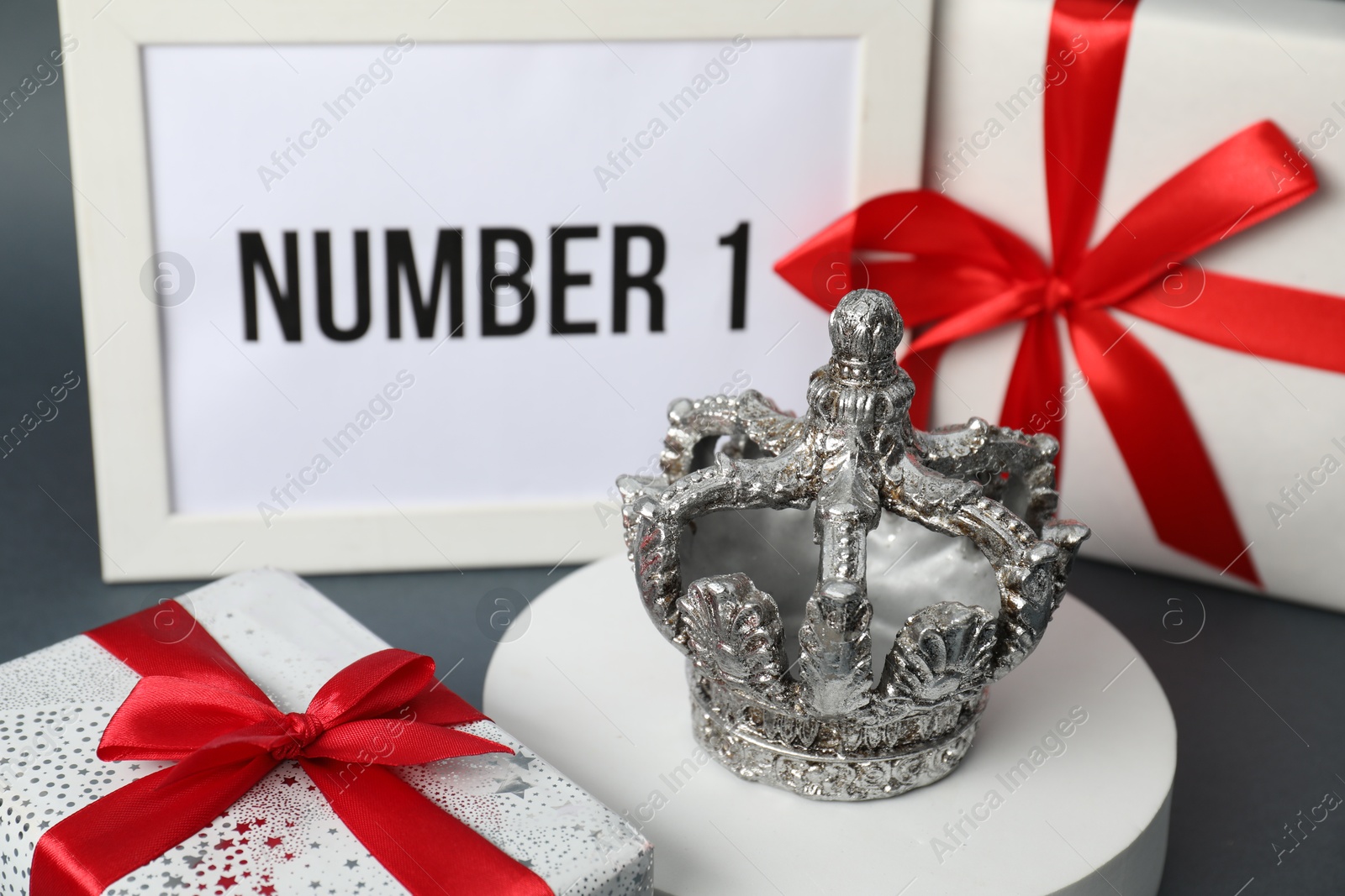 Photo of Crown, frame with phrase Number 1 and gift boxes on grey table, closeup