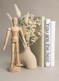 Photo of Wooden human figure, vase with decorative plants and white book with sentence You are the best between ones on light grey background