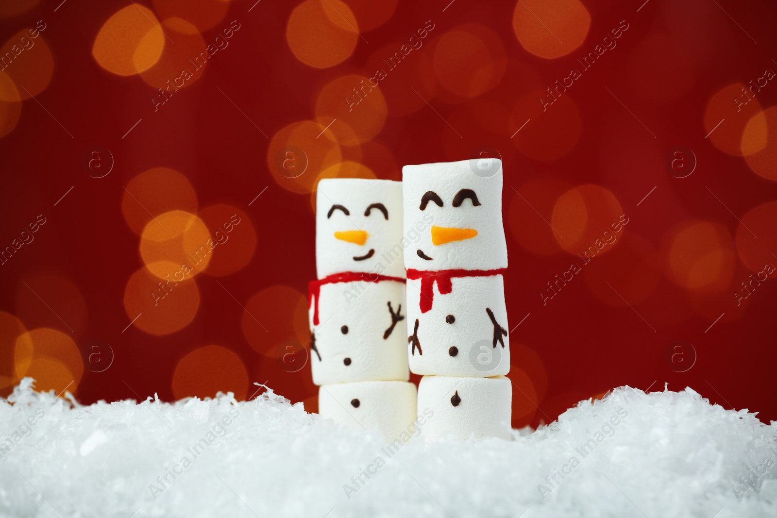 Photo of Funny snowmen made with marshmallows on artificial snow against blurred festive lights