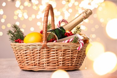 Photo of Wicker gift basket with sparkling wine and Christmas decor on light textured table