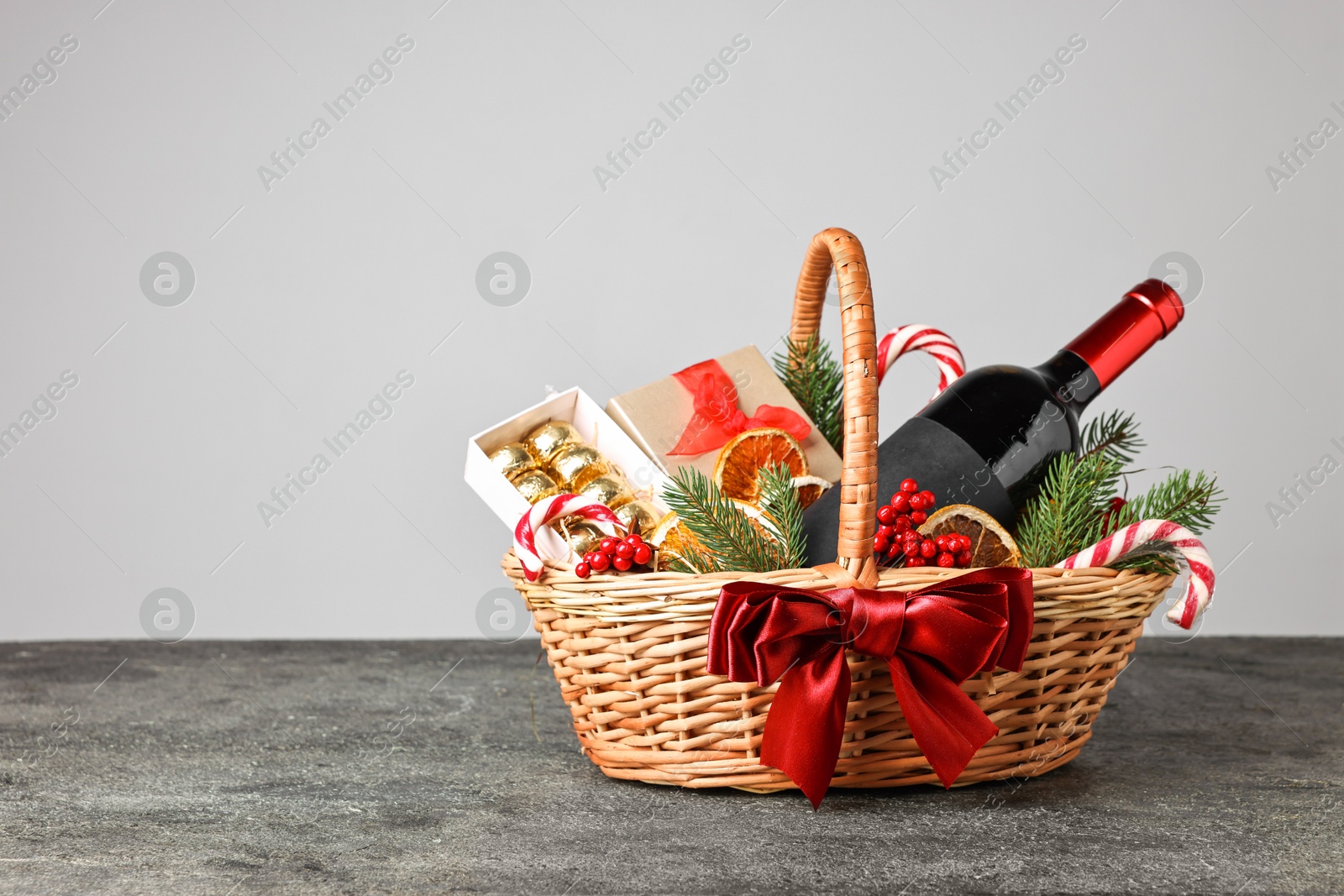 Photo of Wicker gift basket with wine and Christmas decor on grey textured table, space for text