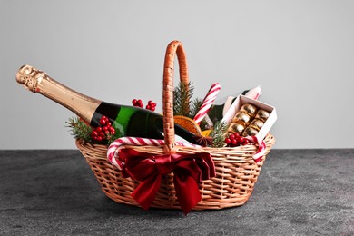 Photo of Wicker gift basket with sparkling wine and Christmas decor on grey textured table