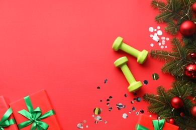 Photo of Dumbbells, fir tree branches, Christmas baubles and gift boxes on red background, flat lay. Space for text