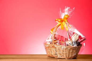 Photo of Wicker gift basket with wine on wooden table against pink background, space for text