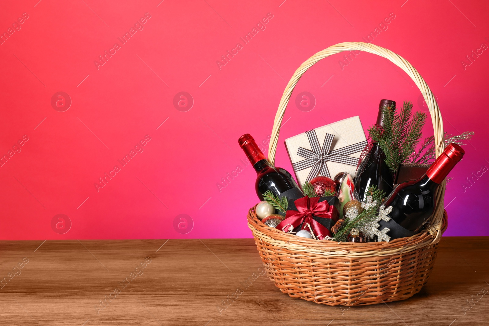 Photo of Wicker gift basket with wine on wooden table against pink background, space for text