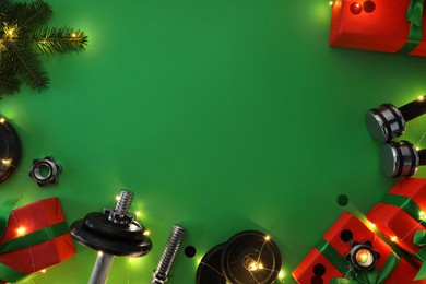 Photo of Dumbbells, fir tree branches, gift boxes and Christmas lights on green background, flat lay. Space for text