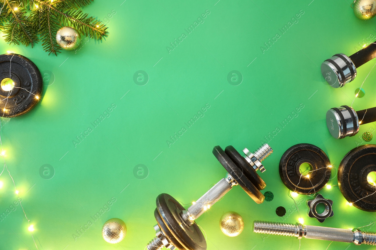 Photo of Dumbbells, fir tree branches, baubles and Christmas lights on green background, flat lay. Space for text