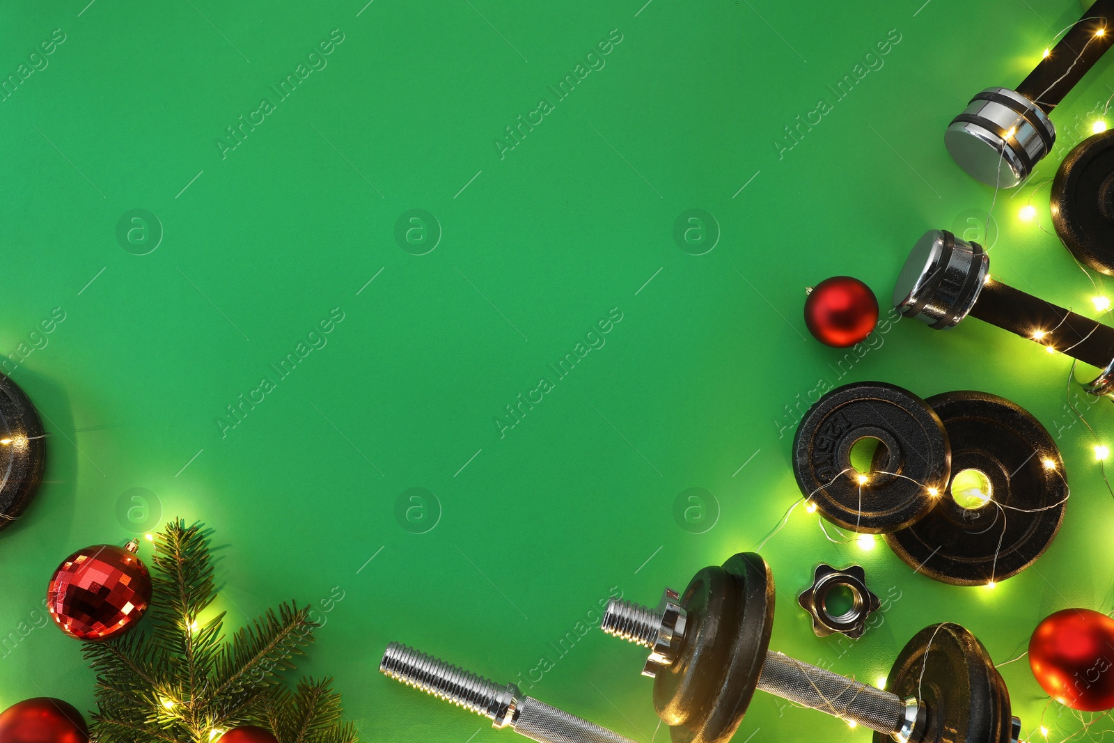 Photo of Dumbbells, fir tree branches, baubles and Christmas lights on green background, flat lay. Space for text