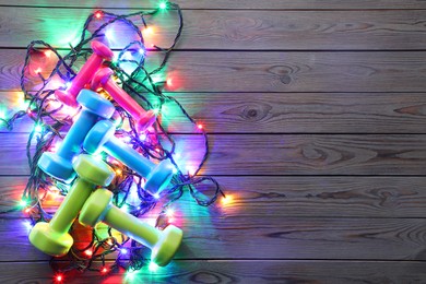 Photo of Dumbbells, and Christmas lights on wooden table, top view. Space for text