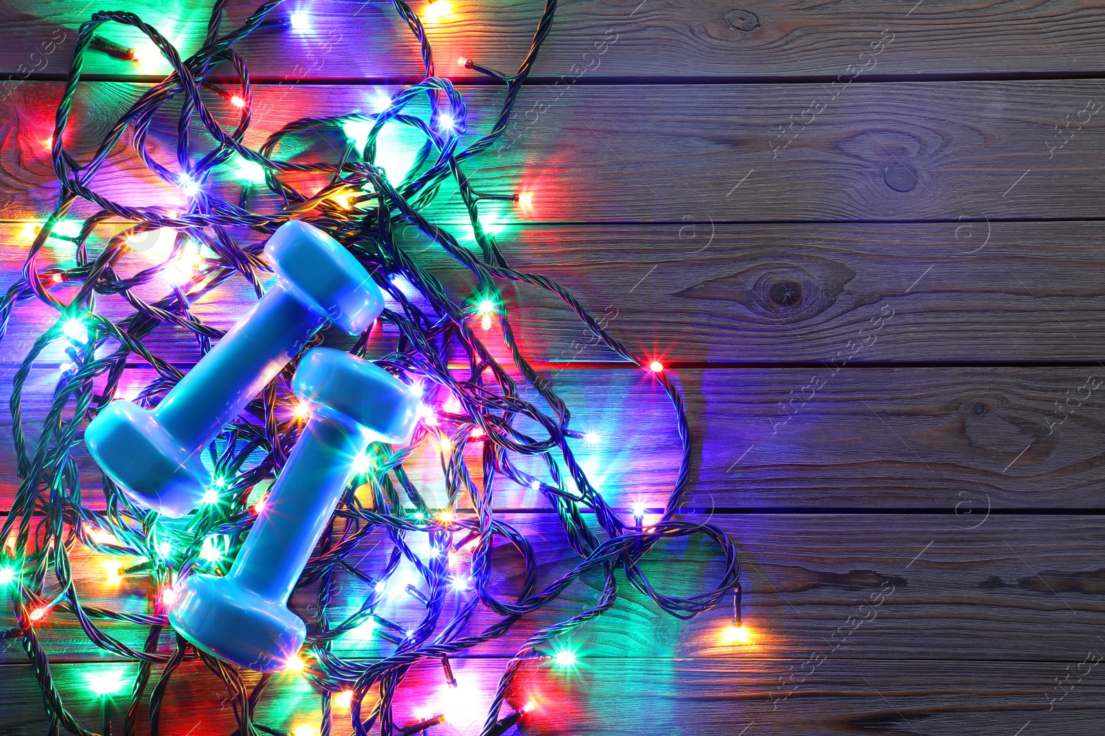 Photo of Dumbbells, and Christmas lights on wooden table, top view. Space for text