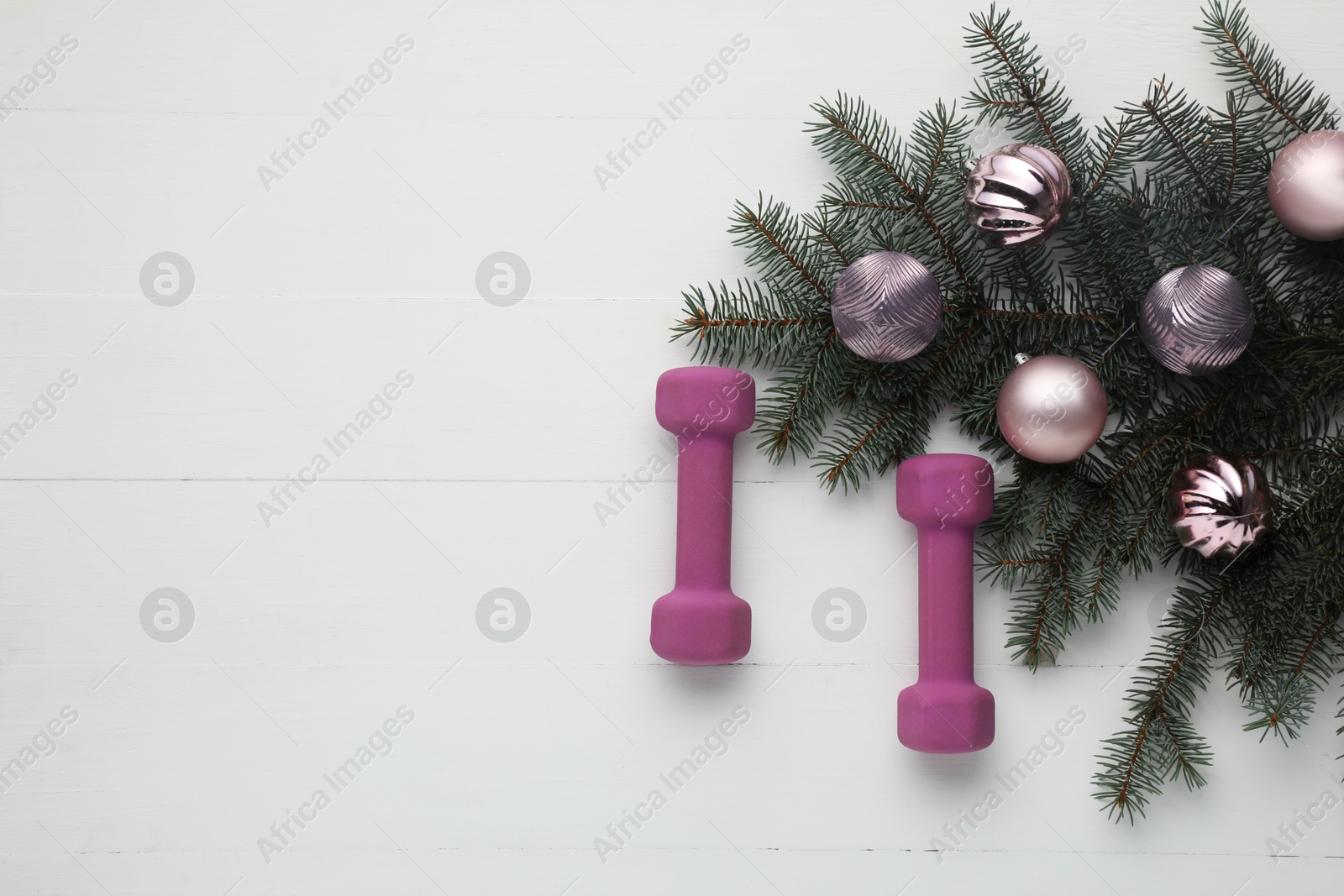 Photo of Dumbbells, fir tree branches and Christmas baubles on white table, flat lay. Space for text