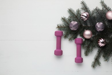 Photo of Dumbbells, fir tree branches and Christmas baubles on white table, flat lay. Space for text