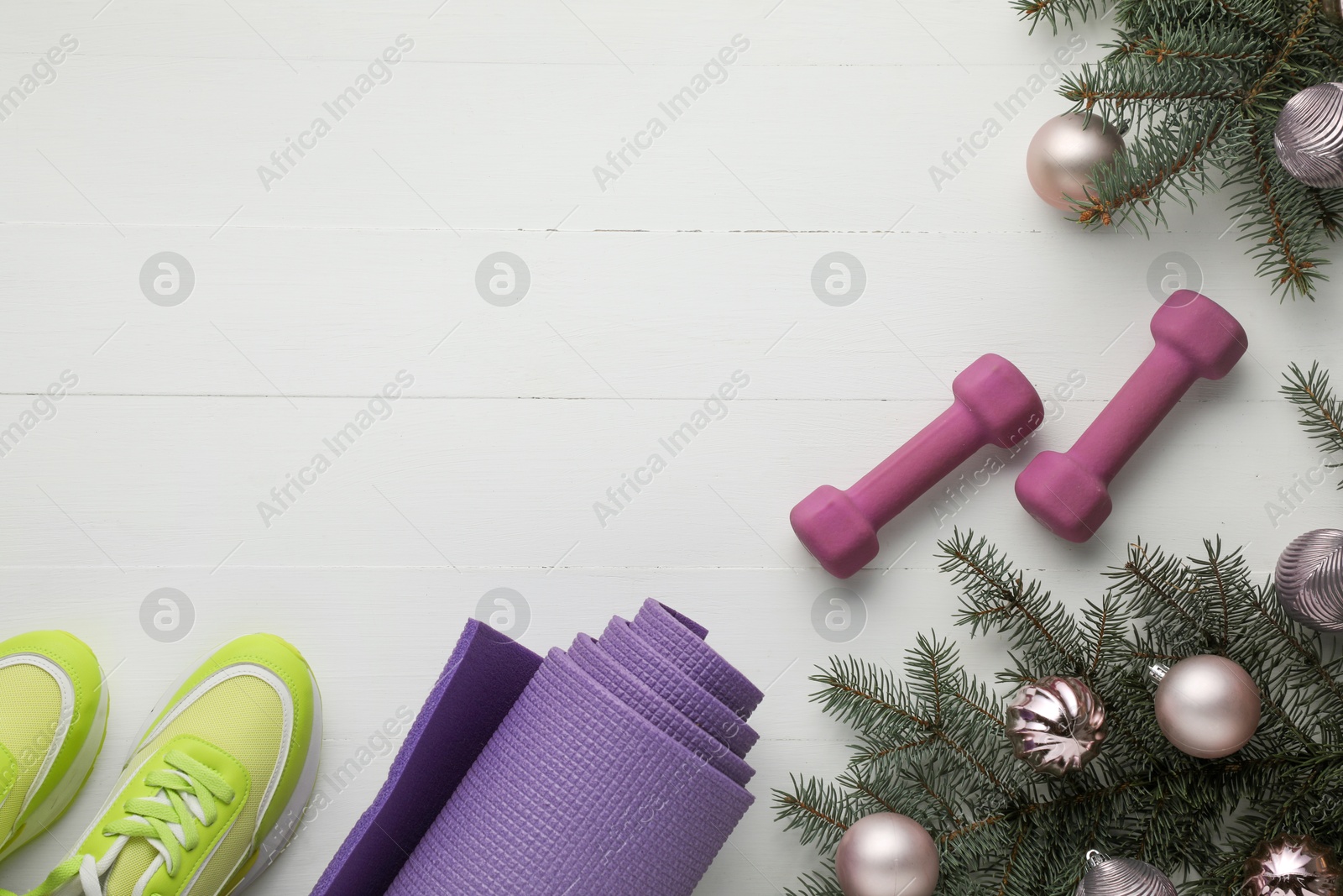 Photo of Dumbbells, mat, sneakers, fir tree branches and Christmas baubles on white table, flat lay. Space for text