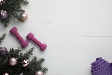 Photo of Dumbbells, mat, fir tree branches and Christmas baubles on white table, flat lay. Space for text