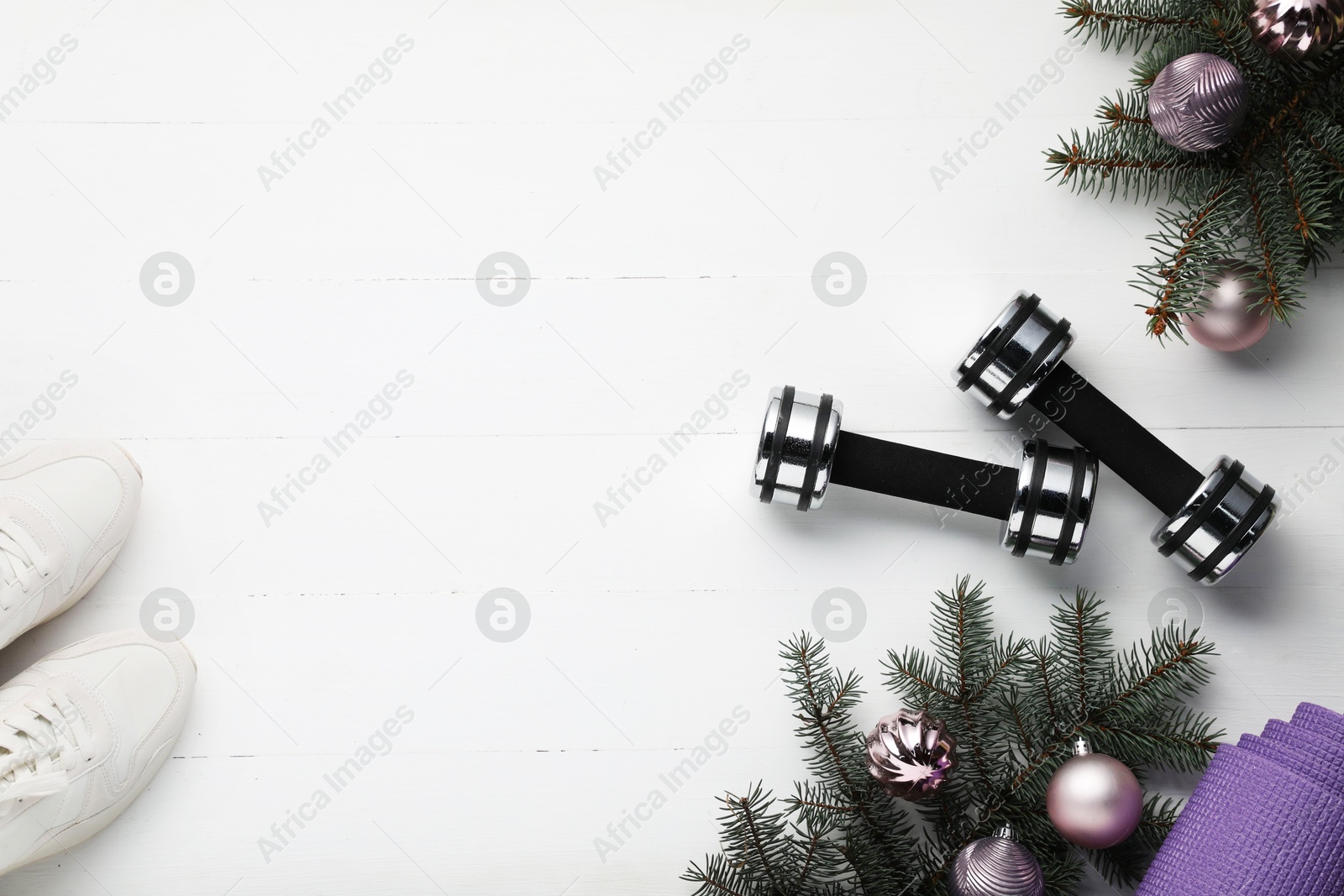 Photo of Dumbbells, mat, sneakers, fir tree branches and Christmas baubles on white table, flat lay. Space for text