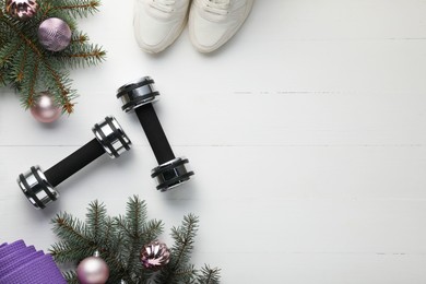 Photo of Dumbbells, mat, sneakers, fir tree branches and Christmas baubles on white table, flat lay. Space for text