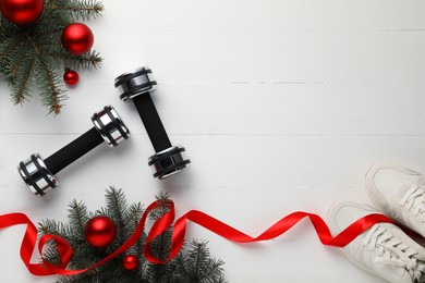 Photo of Dumbbells, sneakers, fir tree branches and Christmas baubles on white table, flat lay. Space for text