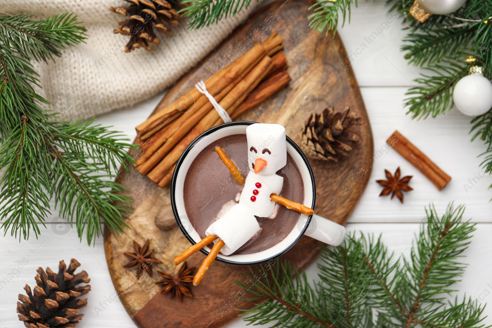 Photo of Funny snowman made with marshmallows in cup of hot chocolate and winter decor on white table, flat lay