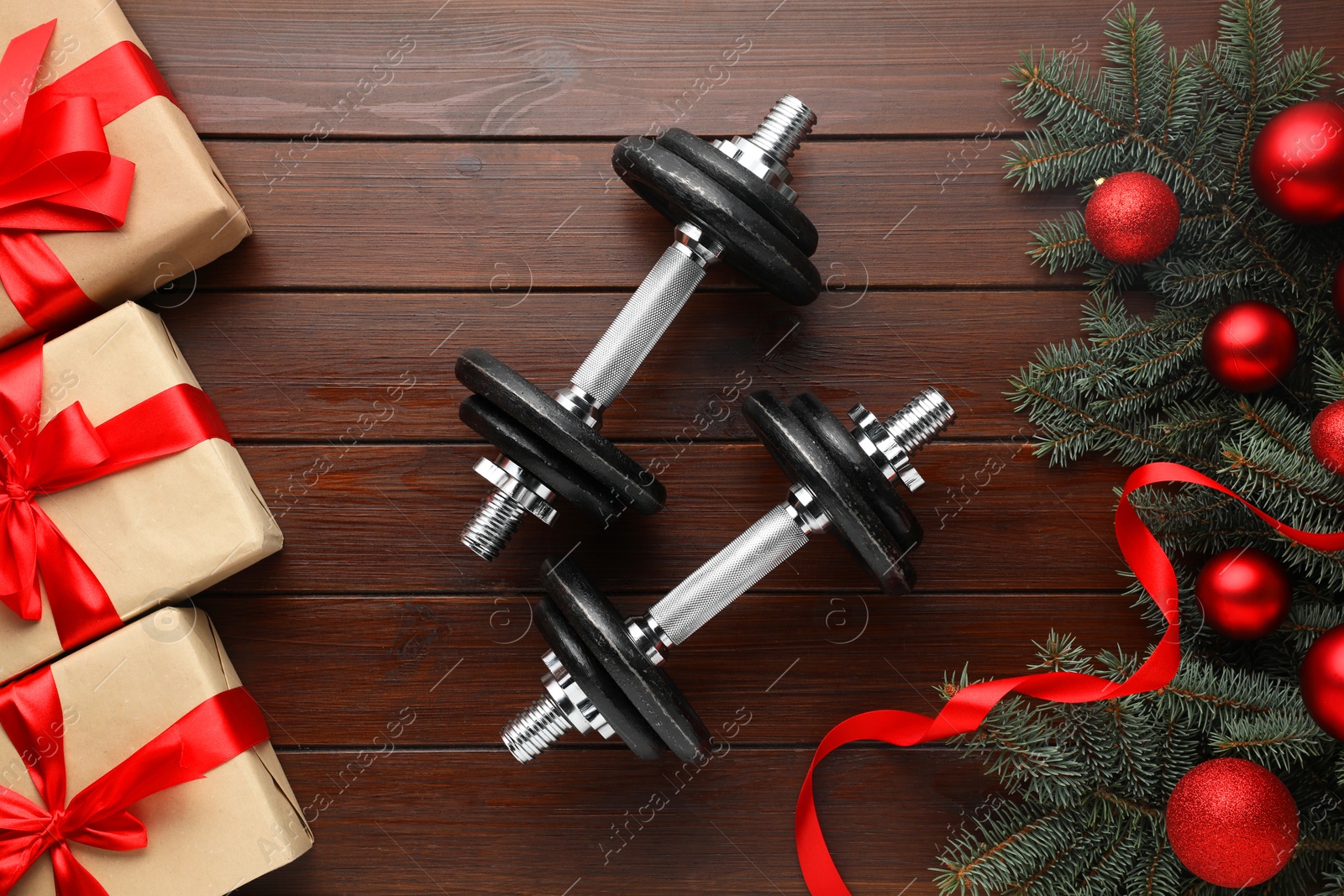 Photo of Dumbbells, fir tree branches, Christmas baubles and gift boxes on wooden table, flat lay