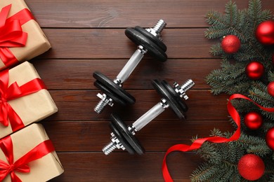 Photo of Dumbbells, fir tree branches, Christmas baubles and gift boxes on wooden table, flat lay